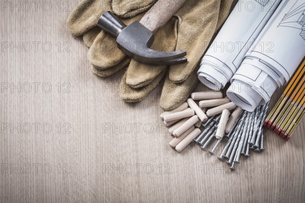 Wooden meter dowels blueprint rolls claw hammer leather protective gloves and metal nails on wood