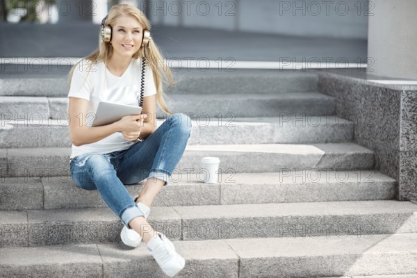 Happy young woman with vintage headphones and a cup of coffee to go, surfing the internet on a
