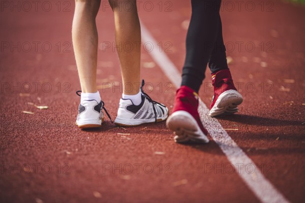 Four legs close-up brother and sister in trainers running on red treadmill in running stadium rear