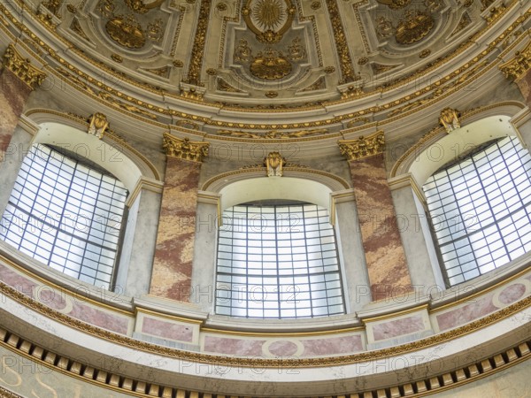 Detailed baroque ceiling with gilded decorations and large windows inside a historic building,