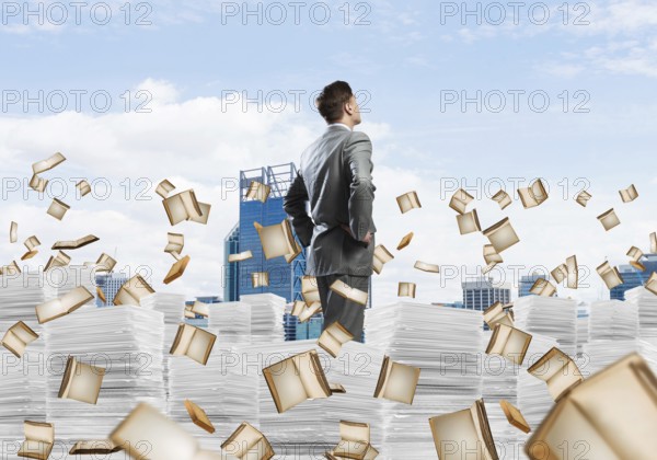 Confident businessman in suit standing on pile of documents among flying books with cityscape on