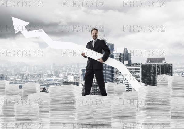 Young and ambitious businessman in suit holding big white arrow in hand and pointing away while