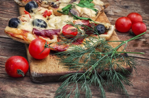 Hunk of delicious meat pizza with bacon and olives on the background of the vegetables.The image is