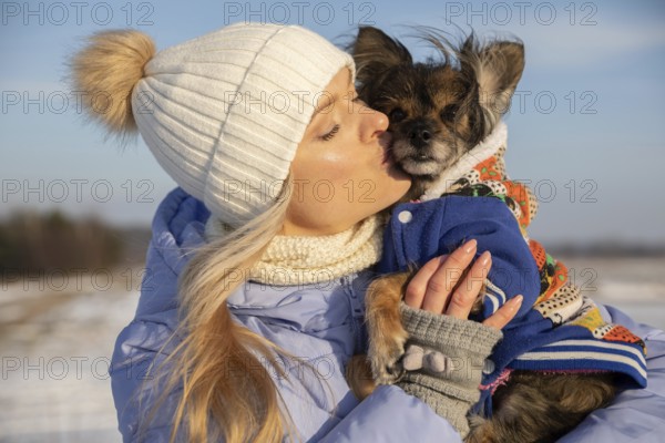 Close-up of a blonde woman hugging her dog. The woman and dog are outside on a winter day. Both are