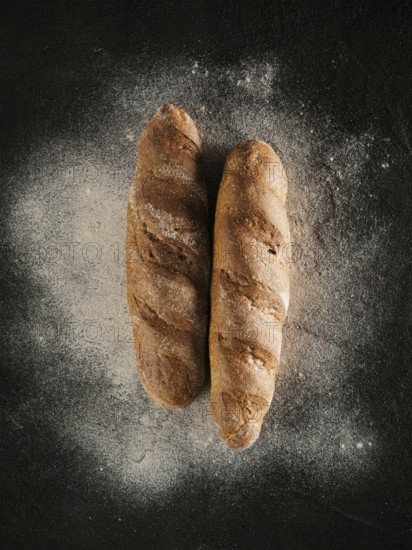 Two whole homemade buckwheat loaf bread with buckwheat flour on black textured background. Top view