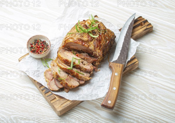 Rolled turkey roasted with spices and herbs on baking paper with knife and wooden white background