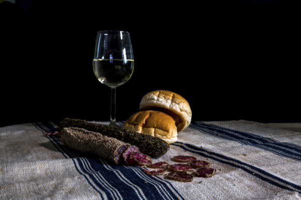 Still life table with a glass of white wine assorted dry sausages and bread on a flour cloth with