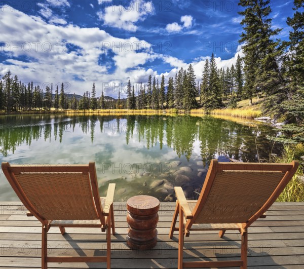 Adorable lake. Two wooden deckchairs for tourists. Coniferous forest is reflected in the mirrored