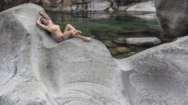 A woman lying in a comfortable position on a smooth granite rock on the bank of a river, Verzasca