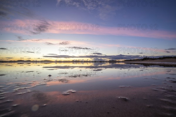Puddle in a dune by the sea. Reflection of the sunrise in the morning. Bay and coast near