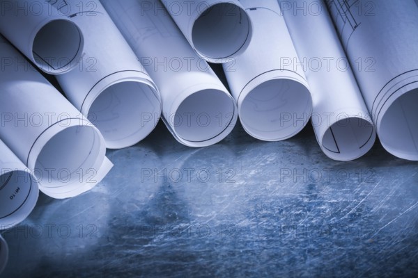 Set of rolled up white construction drawings on scratched silver-metal surface building and
