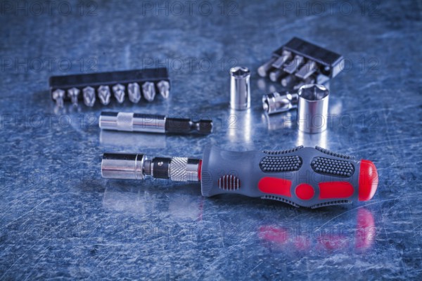 Insulated screwdriver with interchangeable bits and heads on scratched metallic background