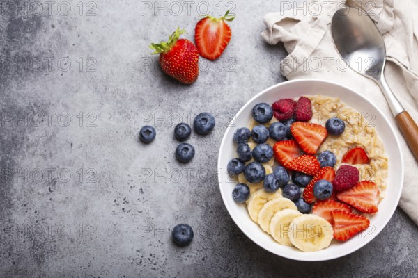 Oatmeal porridge with fruit and berries in bowl with spoon on gray stone background table top view,