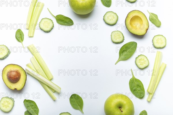 Bottle of green smoothie surrounded by green fruit and vegetables: apples, avocado, spinach, celery