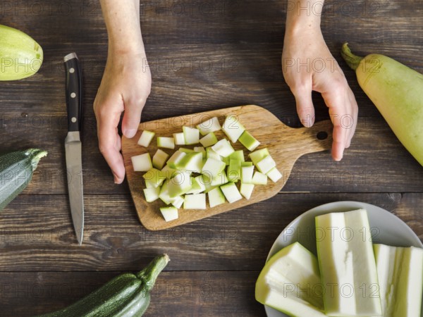 Zucchini harvest. Woman slices zucchini cubes for freezing on wooden table. Farm organic zucchini