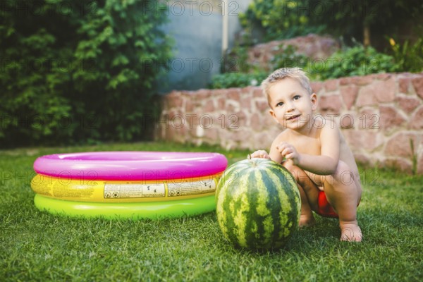 Toddler cute Caucasian white European race boy sitting hugging holding huge watermelon and smiling