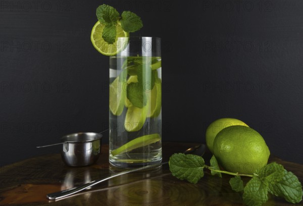Glass of Mojito cocktail with mint and lime on a black board with fresh limes. Sparkling refreshing