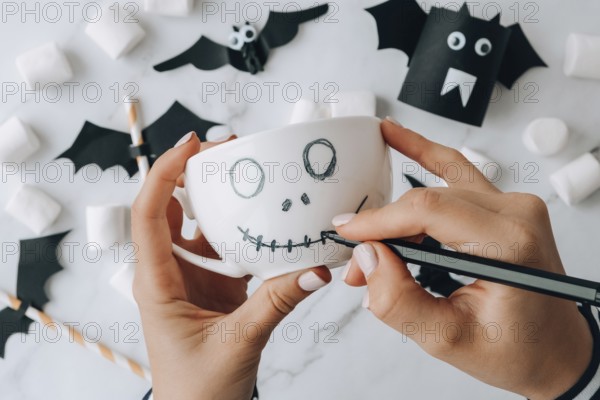 Female hands paint on white cup scary jacks face DIY for kids Halloween home activities Holiday art
