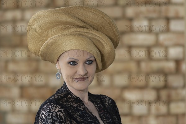 Woman in black lace dress with golden turban in front of beige wall, staged portrait shooting,