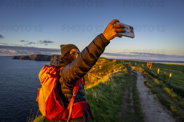Female hiker taking a selfie, Cliffs of Moher, The Burren, County Clare, Ireland, United Kingdom,