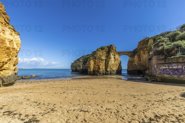 Yellow rocks and cliffs on a sandy beach. A bay by the sea, over which the old stone bridge of the