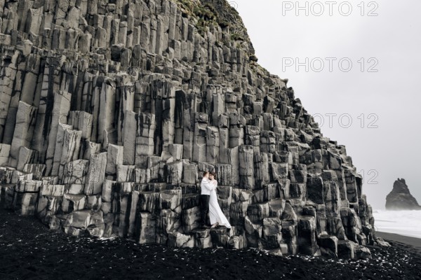A wedding couple stands on a wall of stone pillars. The bride and groom are hugging on basalt