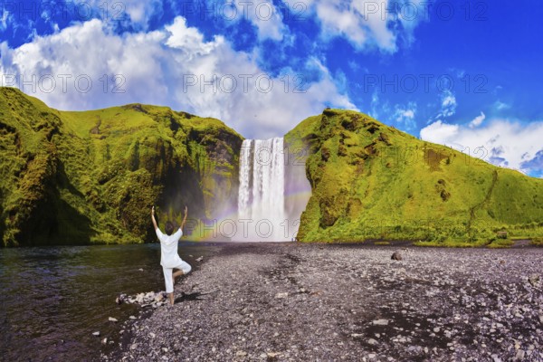 Elderly woman performs asana tree of hatha yoga before falling water. Grand waterfall with rainbow