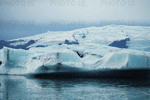 Vast iceberg floating near a glacier under gray skies, iceberg, glacier, snow, ice rock, ice