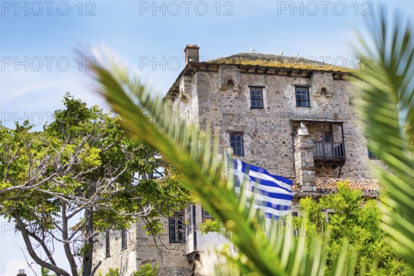Ancient Ouranoupolis Tower on Athos peninsula in Halkidiki, flag of Greece. View through the palm