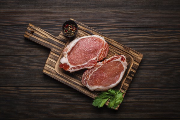 Cut raw meat pork steaks with seasonings on kitchen cutting board, rustic wooden background top
