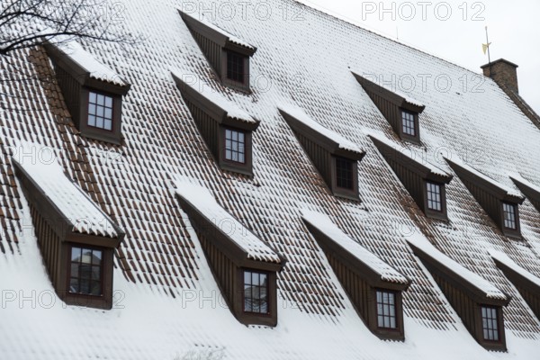 Snow falling on the roofs of the city. Snow-covered brown metal tiles roof of European house with