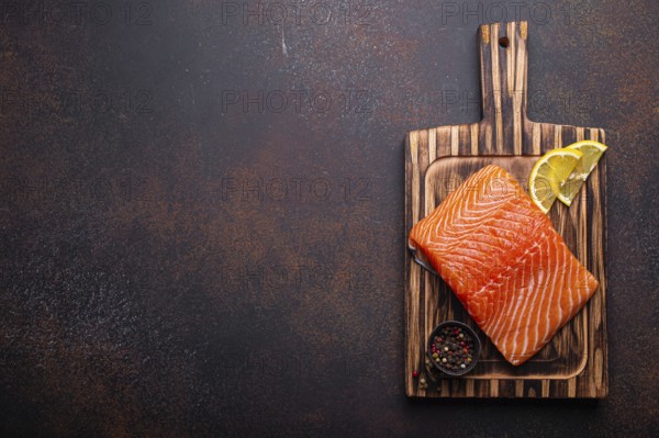 Fresh raw salmon fillet on wooden kitchen cutting board with seasonings and lemon top view on dark