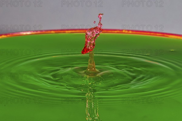 A red water drop rises dynamically on a green background, water drop, collision, high-speed