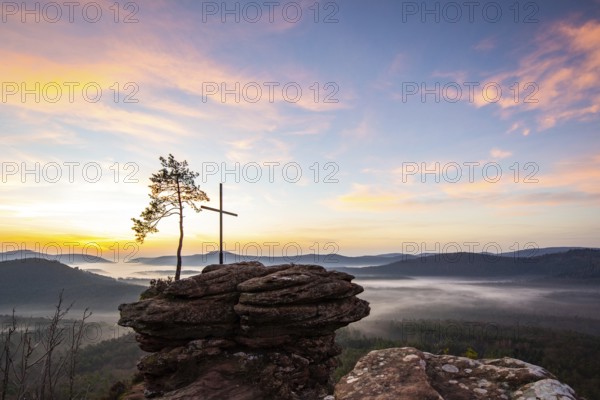 Landscape shot of nature in the morning. Mist in the valley and a summit cross on a sandstone cliff