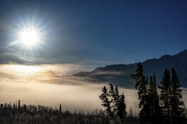 Sun over foggy, snow-covered landscape with mountain silhouette, Yukon, Canada, Kluane National