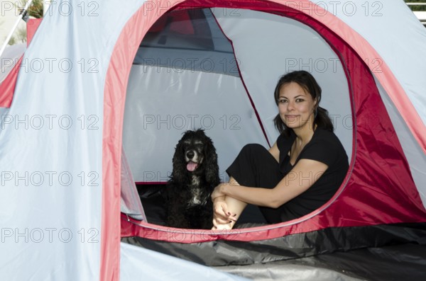 Woman Sitting Inside a Camping Tent with Her Cocker Spaniel Dog in a Sunny Summer Day in