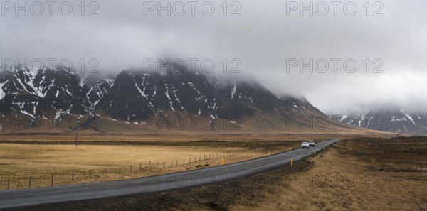 Straight highway country road with cars moving and mountains covered in mist in Iceland. Road is