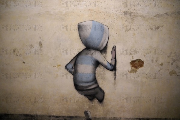 A lonely boy with a hood stands in front of a plain wall, creating a calm and minimalist