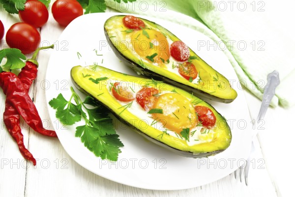 Scrambled eggs with cherry tomatoes in two halves of avocado in a plate, towel and fork on white