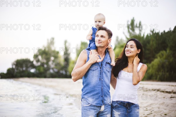 Beautiful young family on holiday with baby. The father holds the blonde girl in her arms, and the