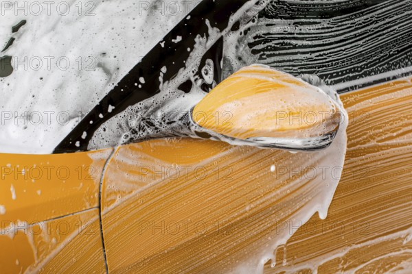 Detail on strokes left by brush in shampoo and foam, front mirror of a car washed in carwash
