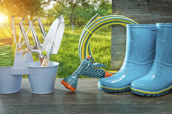 Gardening tools blue rubber rain boots hose sprayer gun spade and fork on vintage table in spring