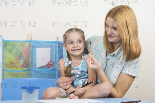 A five-year girl is engaged in drawing with adult young beautiful girl sitting at the children