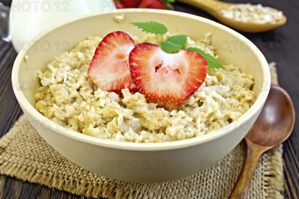 Oatmeal in a yellow cup with strawberries on a napkin of burlap, spoon, milk in a glass jar on the