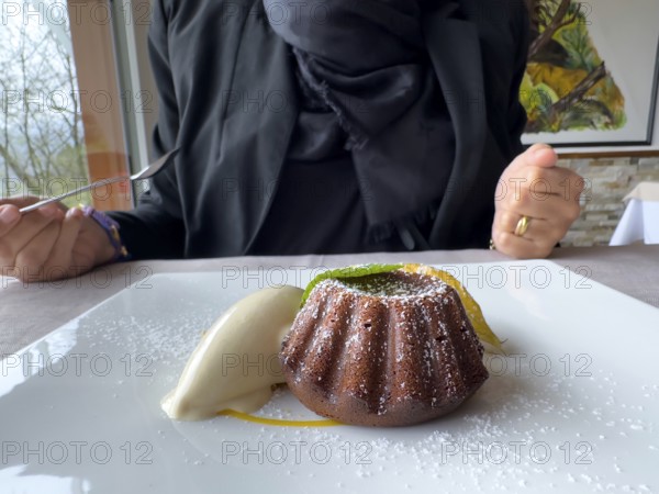 Woman Eating on a White Plate With an Elegant Warm Dark Chocolate Cake Dessert With Vanilla Ice