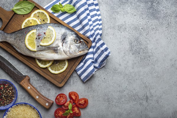 Raw fish dorado with ingredients lemon, fresh basil, cut cherry tomatoes, uncooked rice on wooden