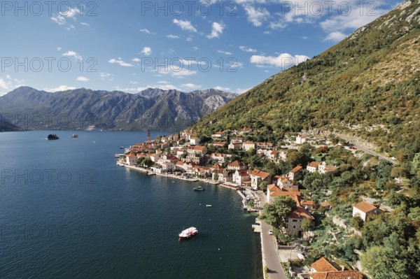 Boat is moored in the bay near the winding shore of Perast with a view of the bell tower.