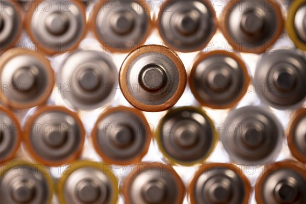Multiple used AA alkaline batteries are seen arranged in a pile. Closeup front view from the plus