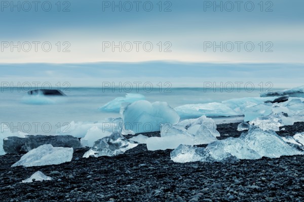 Ice formations along the ocean shoreline under a serene blue sky, creating a cold feeling,
