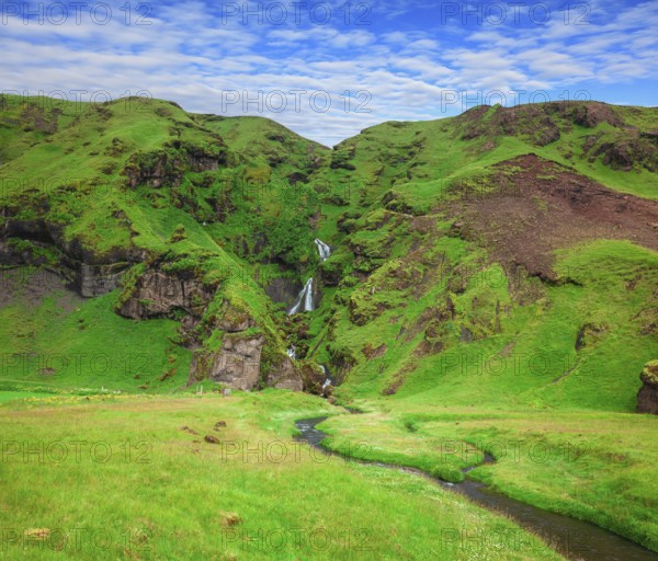 Basalt mountains covered in green moss and grass . Gorgeous cascading waterfall from melting